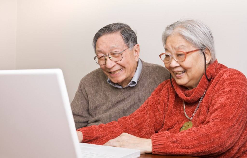 Asian husband and wife sit at desk looking at computer