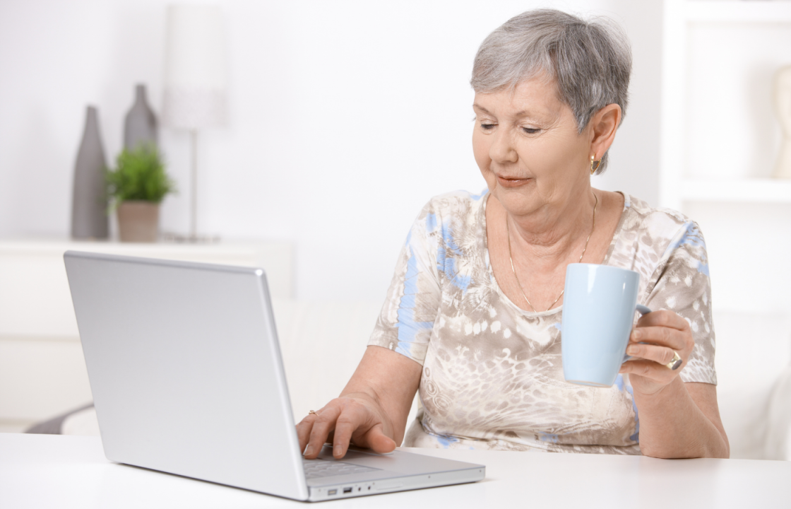 senior white female sitting at computer with mug in her hand