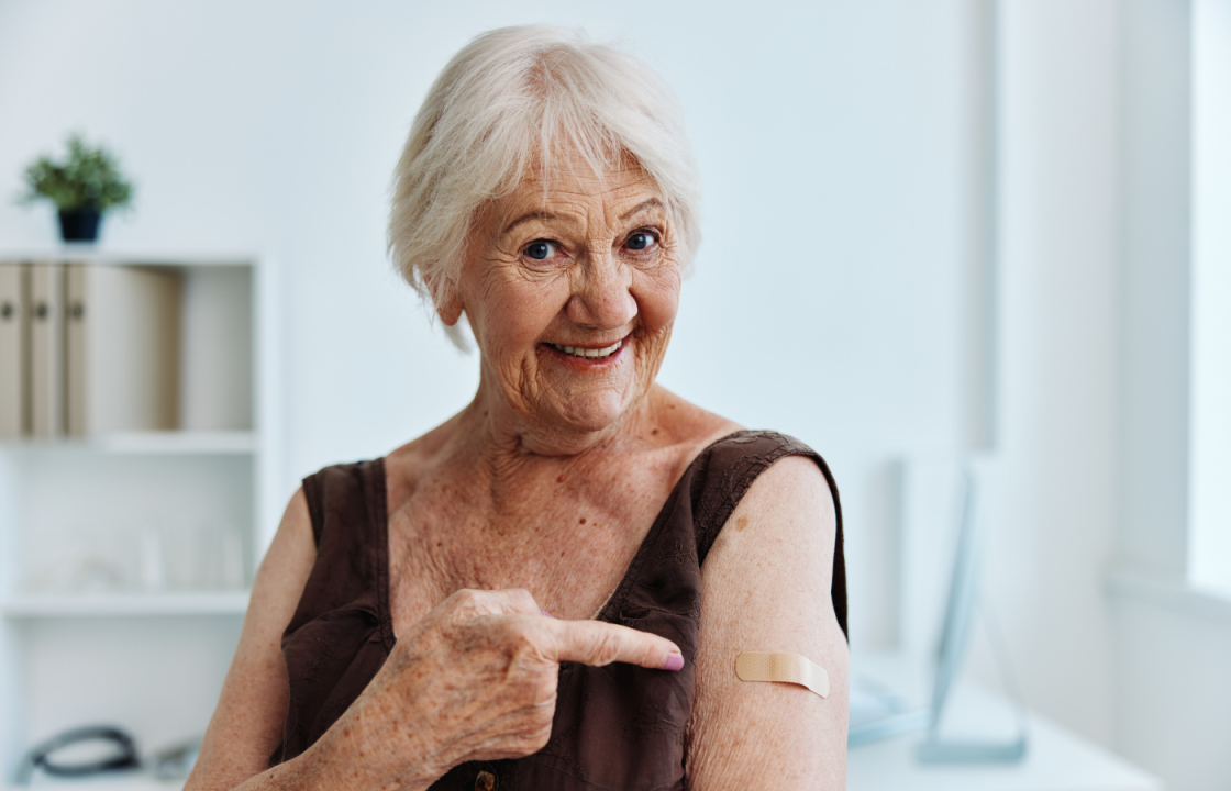 older white female smiles and point at bandaid on arm