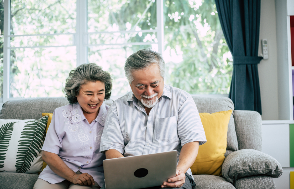 Older asian husband and wife sitting on couch looking at computer