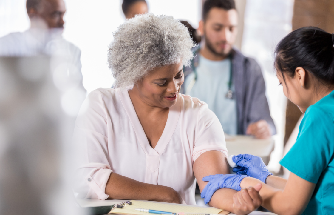 black older woman gets flu shot from younger female healthcare worker