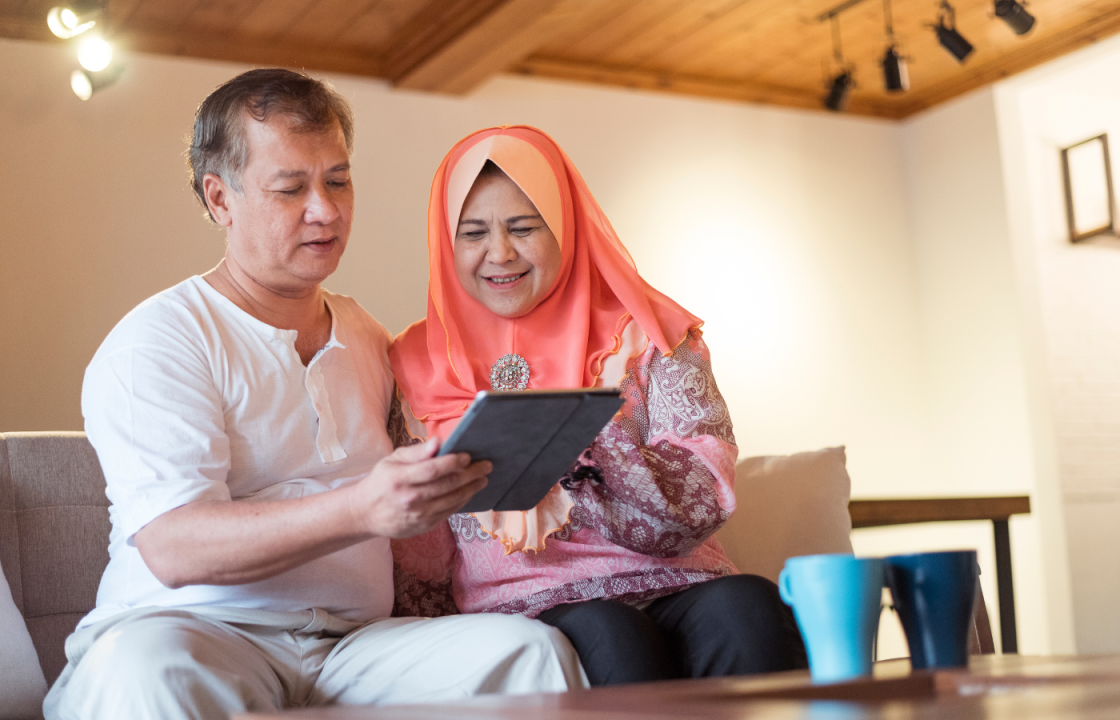Asian couple sitting on couch looking at tablet in their hands