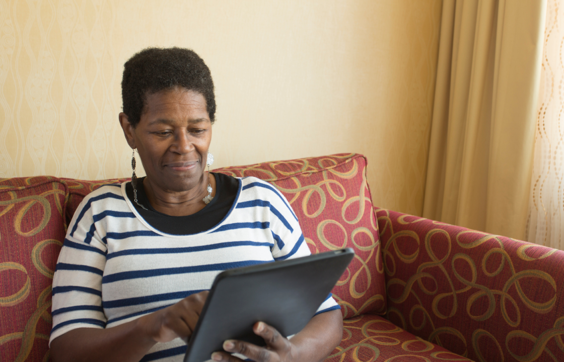 Black older woman sitting on couch looking at tablet in her hand