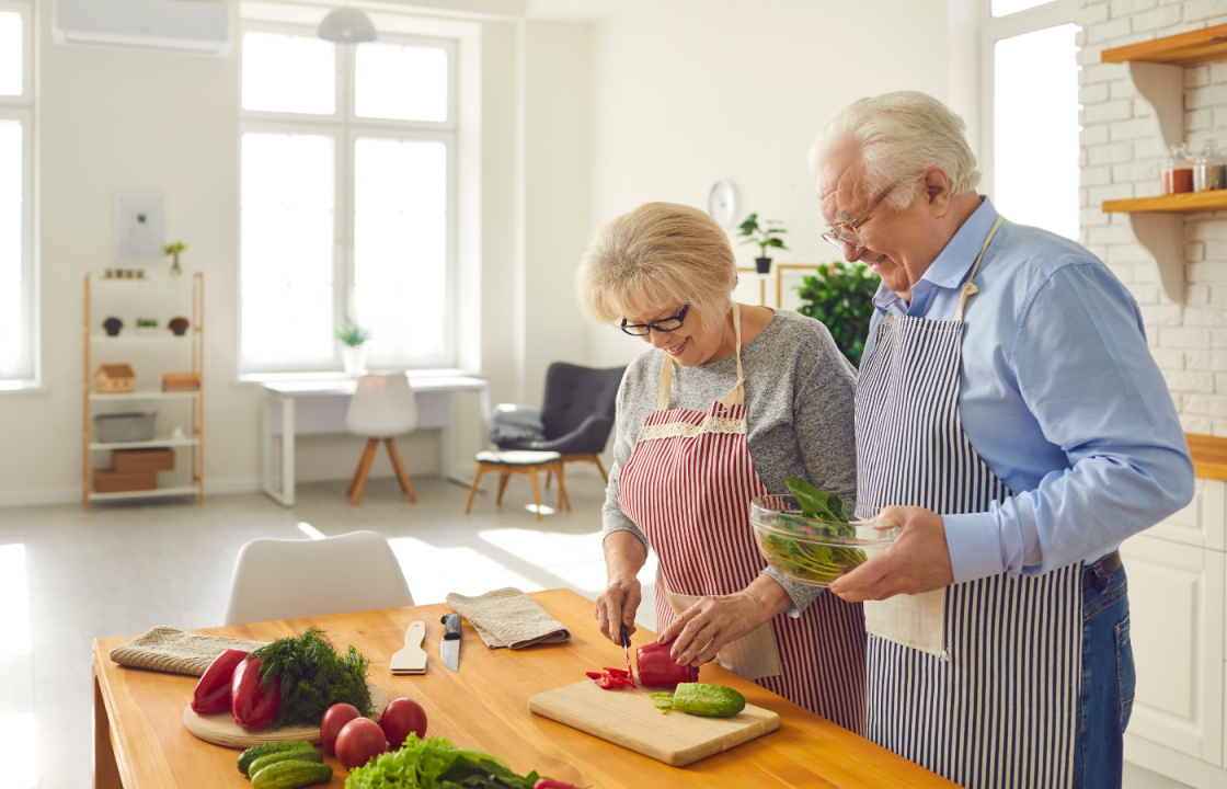 white older husband and wife cutting veggies in a large kitchen